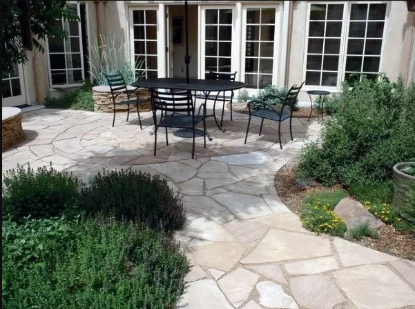 Triple R Landscaping designs and installs hardscapes like this beautiful flagstone walkway and patio in light earth tones with steps going down to planting areas.