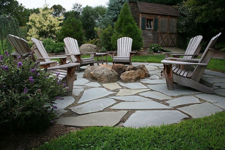 natural large boulder fire pit with large flagstone surround and outdoor chairs in a circle around it